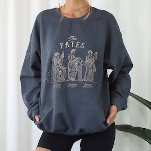 May include: A dark blue sweatshirt with a graphic of the three Fates, Clotho, Lachesis, and Atropos, from Greek mythology. The text "The Fates" is printed above the graphic.
