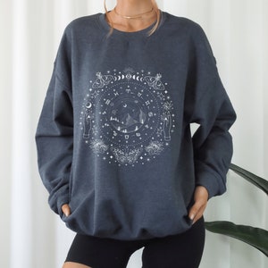 May include: A dark gray sweatshirt with a white graphic print of a celestial design featuring moons, stars, zodiac symbols, and butterflies.