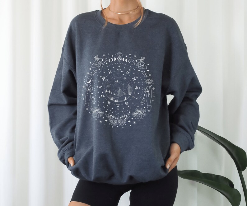 May include: A dark gray sweatshirt with a white graphic print of a celestial design featuring moons, stars, zodiac symbols, and butterflies.
