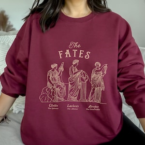 May include: Burgundy sweatshirt with a graphic of the three Fates, Clotho, Lachesis, and Atropos, with their names and titles below. The graphic is in a gold outline.
