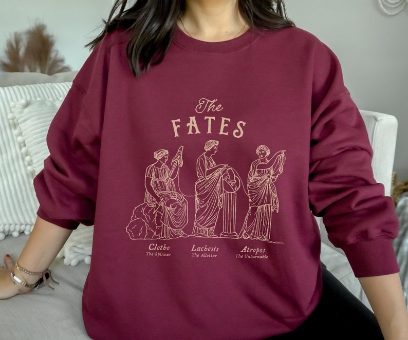 May include: Burgundy sweatshirt with a graphic of the three Fates, Clotho, Lachesis, and Atropos, with their names and titles below. The graphic is in a gold outline.