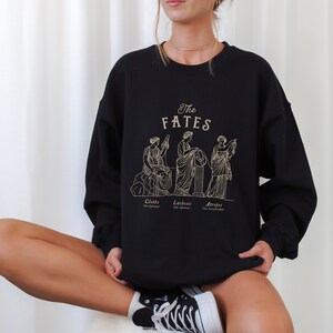 May include: Black sweatshirt with a graphic print of three women, labeled "The Fates" with their names and titles: Clotho, The Spinner, Lachesis, The Allotter, and Atropos, The Inevitable.
