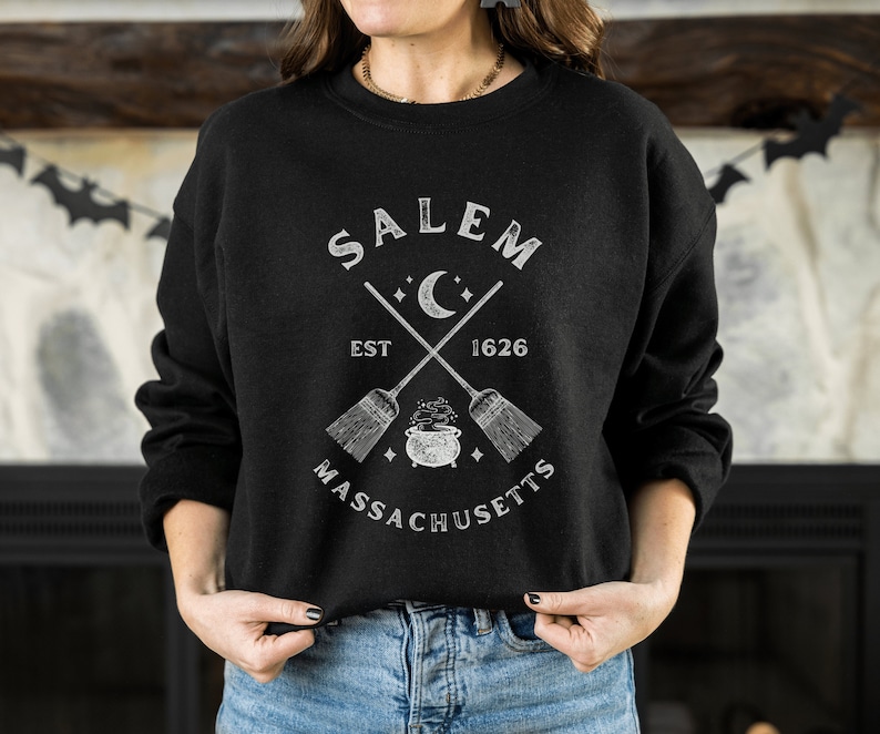 May include: Black sweatshirt with a white graphic design featuring the text "SALEM EST 1626 MASSACHUSETTS" with a crescent moon and crossed broomsticks.