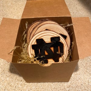 May include: A set of wooden coasters with a black Notre Dame logo, packaged in a brown cardboard box with shredded paper.