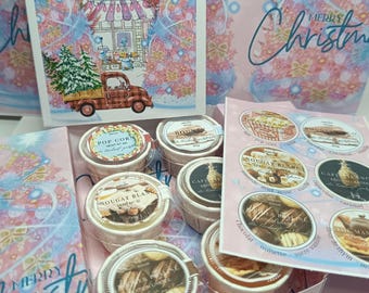 May include: A Christmas gift set featuring a box with several small, round containers of treats. The box includes a card with a Christmas scene and the words "Merry Christmas". The containers have labels with various flavors.