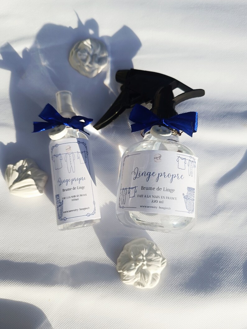 May include: Two clear glass spray bottles with blue ribbon bows and labels that read "Linge propre" in French. The labels also say "Brume de Linge" and "Fait a la main en France".