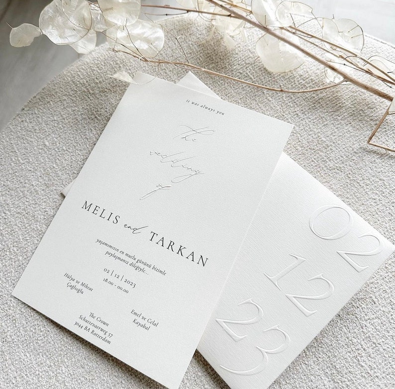 Pode incluir: Um convite de casamento branco com o texto "MELIS e TARKAN" e a data "02/12/2023". O convite tamb&eacute;m inclui o texto "It was always you" e o endere&ccedil;o "The Crows, Schuttevarrweg 57, 3244 BA Rotterdam".