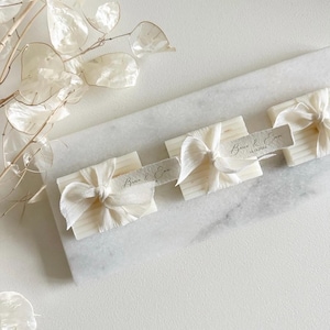 Op de afbeelding: Drie witte zeepjes met een wit lint om elk zeepje gebonden. Elk zeepje heeft een klein wit label met de tekst "Brian & Erin" geschreven in zwarte kalligrafie.