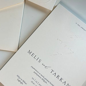 Pode incluir: Um convite de casamento branco com texto preto. O convite diz "MELIS e TARKAN" e inclui a data "02 | 12 | 2023" e a hora "18.00 - 00.00". O convite tamb&eacute;m inclui a localiza&ccedil;&atilde;o "The Crown, Schuttevaerweg 57, 3044 BA Rotterdam" e os nomes "Emel e Celal Kayabal".
