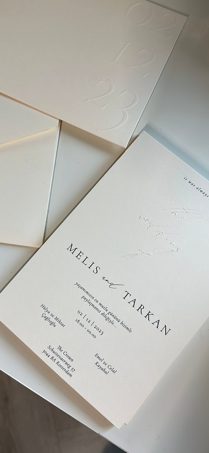 Pode incluir: Um convite de casamento branco com texto preto. O convite diz "MELIS e TARKAN" e inclui a data "02 | 12 | 2023" e a hora "18.00 - 00.00". O convite tamb&eacute;m inclui a localiza&ccedil;&atilde;o "The Crown, Schuttevaerweg 57, 3044 BA Rotterdam" e os nomes "Emel e Celal Kayabal".