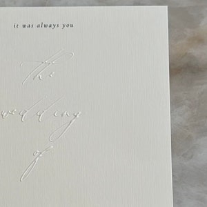 Pode incluir: Um convite de casamento branco com texto preto. O texto diz "it was always you" e "S and TARKAN". A data do casamento est&aacute; indicada como "02 | 12 | 2023" e a hora &eacute; "18.00 - 00.00". Os nomes "Mihrat" e "Emel ve Celal Kayabal" tamb&eacute;m est&atilde;o listados.