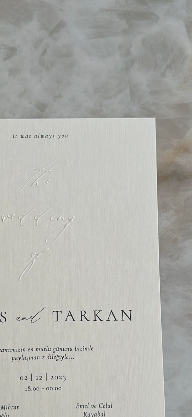 Pode incluir: Um convite de casamento branco com texto preto. O texto diz "it was always you" e "S and TARKAN". A data do casamento est&aacute; indicada como "02 | 12 | 2023" e a hora &eacute; "18.00 - 00.00". Os nomes "Mihrat" e "Emel ve Celal Kayabal" tamb&eacute;m est&atilde;o listados.
