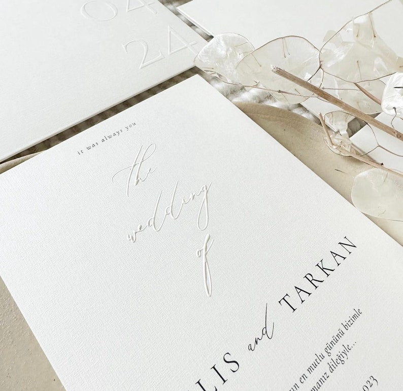 Pode incluir: Convite de casamento branco com texto em relevo que diz "It was always you. The wedding of [name] and [name]" e a data "2023".