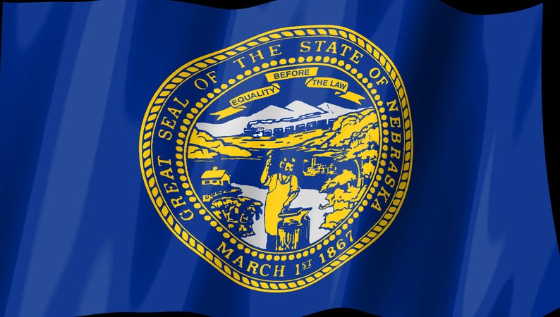 May include: The state flag of Nebraska features a deep blue field with the Great Seal of the State of Nebraska centered in gold. The seal depicts a blacksmith at an anvil, a train, mountains, and a banner reading EQUALITY BEFORE THE LAW.