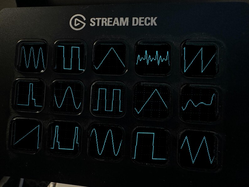 Op de afbeelding: Een zwarte Stream Deck-bedieningsconsole met vijftien vierkante toetsen in een raster. Elke toets toont een unieke, lichtgevende cyaan golfvormgrafiek tegen een donkere achtergrond, die verschillende elektronische signalen en audiofrequenties weergeeft.