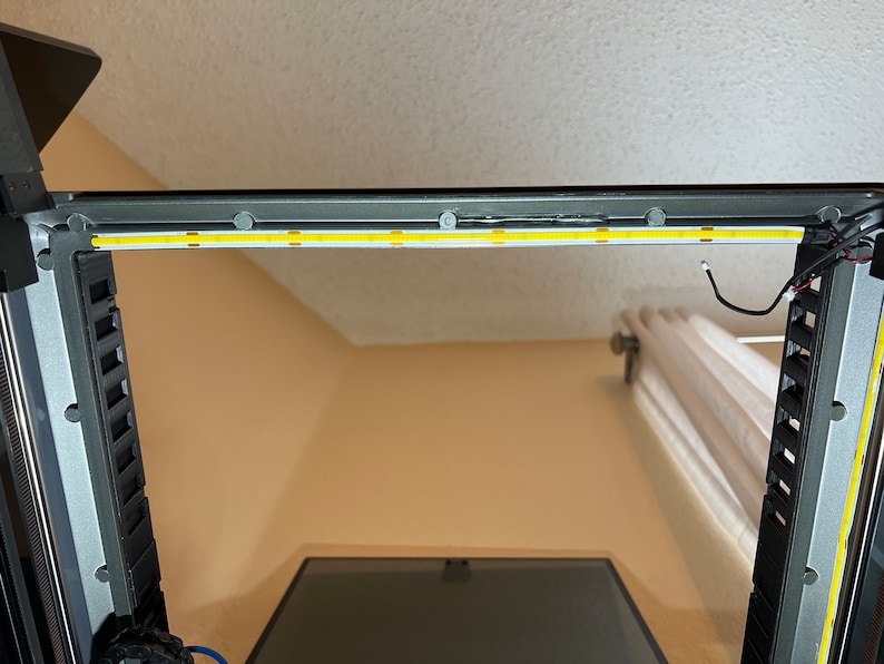 Op de afbeelding: Een close-up van een 3D-printer met een witte LED-lichtstrip die op het bovenste frame is ge&iuml;nstalleerd. De lichtstrip is bevestigd met kleine zelfklevende pads.