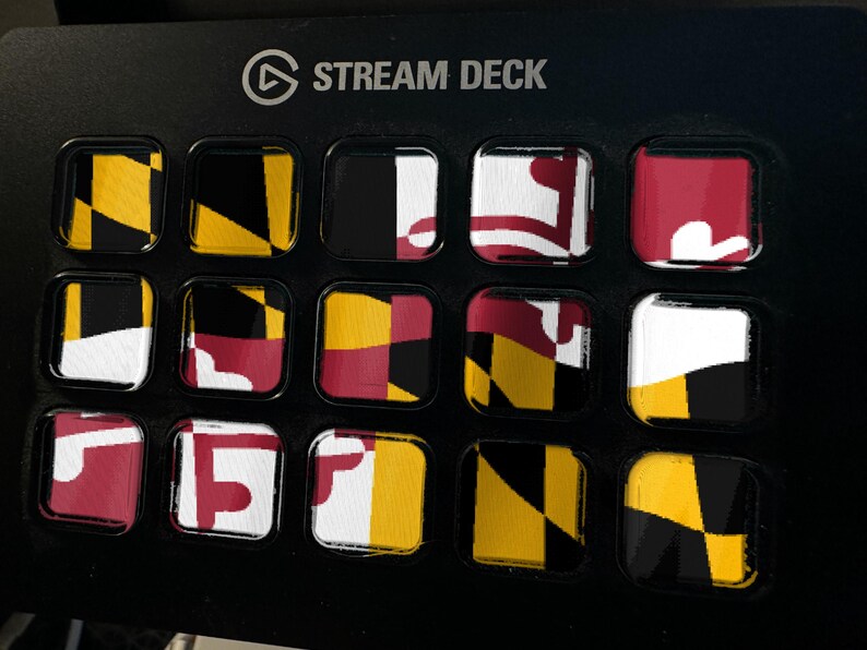 K&ouml;nnte beinhalten: Ein schwarzer Stream Deck-Controller mit f&uuml;nfzehn quadratischen Tasten in einem Raster. Jede Taste zeigt einen Teil der Flagge des Bundesstaates Maryland, die sich durch ihre markanten schwarzen, goldenen, wei&szlig;en und roten geometrischen Muster auszeichnet.