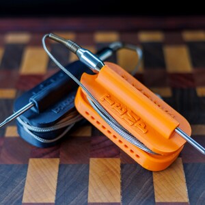 May include: Two food thermometers with stainless steel probes. One is orange and the other is black. The orange thermometer has the word "TEMP" printed on it. Both thermometers have a wire attached to the probe.