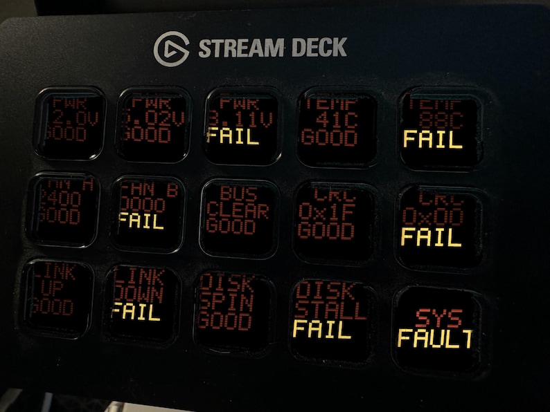 May include: A black Elgato Stream Deck control console featuring a grid of fifteen square LCD keys. The keys display various system status indicators in red and yellow text, including labels like PWR, TEMP, FAN, BUS, LINK, DISK, and SYS FAULT.