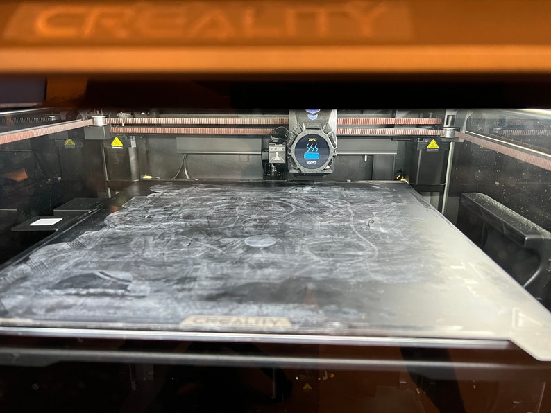 Op de afbeelding: Een zwarte 3D-printer met een glazen printbed en een digitaal display dat "SSS" toont.