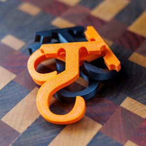 May include: Close-up of several orange and dark blue plastic letter "J" shaped objects. The objects are stacked on top of each other. The background is a wooden surface with a geometric pattern.