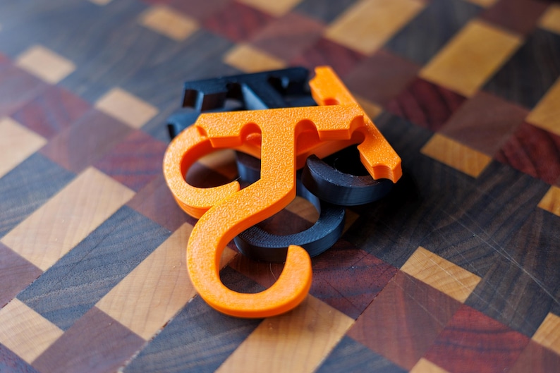 May include: Close-up of several orange and dark blue plastic letter "J" shaped objects. The objects are stacked on top of each other. The background is a wooden surface with a geometric pattern.
