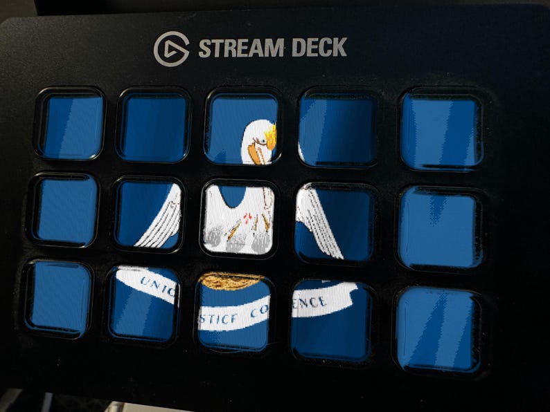 Pode incluir: Um controlador Stream Deck preto com quinze bot&otilde;es quadrados dispostos em uma grade. Os bot&otilde;es exibem uma imagem fragmentada da bandeira do estado da Louisiana, mostrando um pelicano branco, um ninho e uma faixa com o texto Union Justice Confidence.