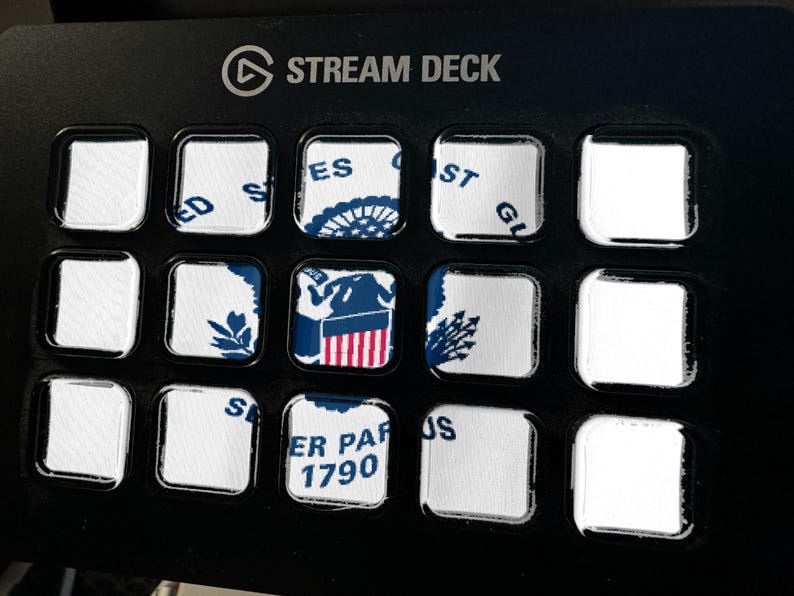 Op de afbeelding: Een zwart Stream Deck bedieningspaneel met vijftien vierkante knoppen. Verschillende knoppen tonen delen van het embleem en de tekst van de United States Coast Guard, waaronder 'United States Coast Guard' en 'Semper Paratus 1790', terwijl andere leeg zijn.