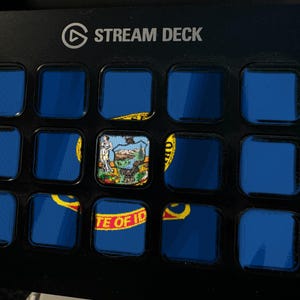 K&ouml;nnte beinhalten: Ein schwarzer Stream Deck-Controller mit einem Raster aus f&uuml;nfzehn quadratischen Tasten. Die Tasten zeigen ein fragmentiertes Bild der Flagge des US-Bundesstaates Idaho, wobei die mittlere Taste das Staatssiegel und die untere Reihe den Text STATE OF IDAHO zeigt.