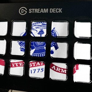 May include: A black Elgato Stream Deck controller featuring fifteen square LCD keys. The keys display a fragmented graphic of the United States Army seal, including the text 'UNITED STATES ARMY' and '1775' in blue and red on a white background.