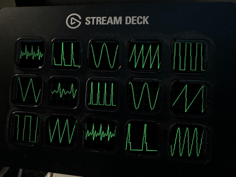 May include: A black Stream Deck controller featuring fifteen square keys arranged in a grid. Each key displays a unique, glowing green waveform graphic, including sine, square, triangle, and sawtooth waves against a dark background.