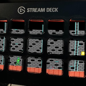 Op de afbeelding: Een zwart Stream Deck-apparaat met vijftien vierkante LCD-toetsen. Elke toets toont een segment van een retro 8-bit videospel-level, met grijze bakstenen muren, oranje vloertegels, blauwe ladders en een klein groen figuurtje.