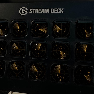 May include: A black Elgato Stream Deck controller featuring fifteen square LCD keys. Each key displays a glowing amber radar screen graphic with circular grid lines and scanning beams. The top of the device is labeled with the text STREAM DECK.