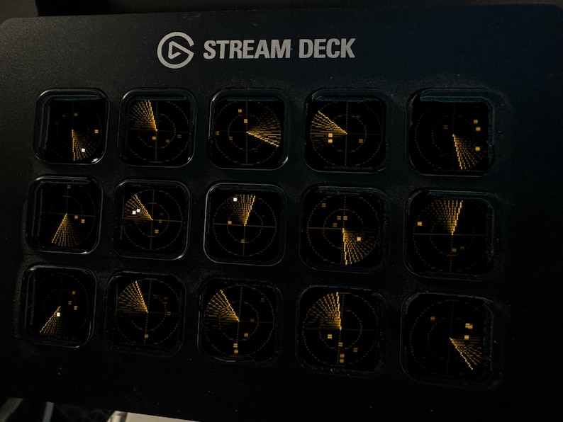 May include: A black Elgato Stream Deck controller featuring fifteen square LCD keys. Each key displays a glowing amber radar screen graphic with circular grid lines and scanning beams. The top of the device is labeled with the text STREAM DECK.