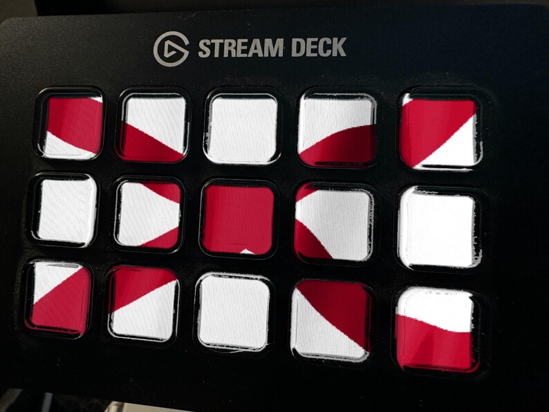 K&ouml;nnte beinhalten: Ein schwarzes Stream Deck Bedienfeld mit f&uuml;nfzehn quadratischen Tasten in einem Raster. Jede Taste zeigt ein rot-wei&szlig;es Grafikmuster. Der Text STREAM DECK ist in Wei&szlig; oben mittig auf dem schwarzen Geh&auml;use des Ger&auml;ts aufgedruckt.