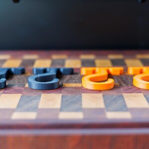 May include: Four 3D-printed hooks in a row. Two are dark gray, and two are bright orange. The hooks are on a wooden surface with a checkerboard pattern of various wood tones.