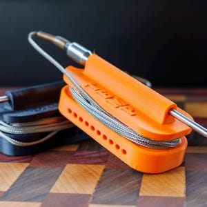 May include: Two temperature probe holders, one black and one bright orange, with stainless steel probes and coiled wires. The orange holder has the word "FASA" printed on it. The holders are designed to keep the probes organized.