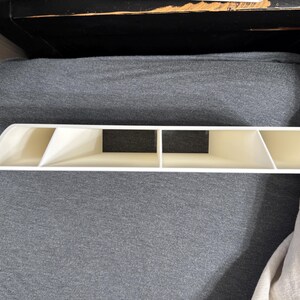 Pu&ograve; includere: Un organizer in plastica bianca con quattro scomparti e un design curvo. L'organizer ha una forma rettangolare con un inserto nero al centro. L'articolo &egrave; posizionato su una superficie grigia.