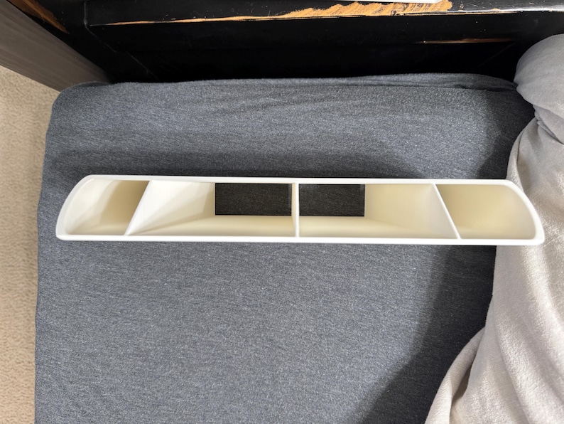 Pu&ograve; includere: Un organizer in plastica bianca con quattro scomparti e un design curvo. L'organizer ha una forma rettangolare con un inserto nero al centro. L'articolo &egrave; posizionato su una superficie grigia.