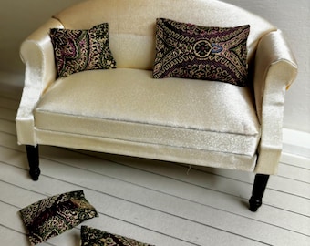 May include: A white velvet tufted sofa with four legs and two pillows with a paisley pattern in shades of green, purple, and gold.