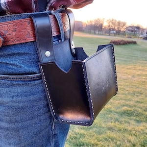 May include: A black leather tool belt with a single pouch hanging from the side. The pouch has white stitching and is secured to the belt with a metal rivet.