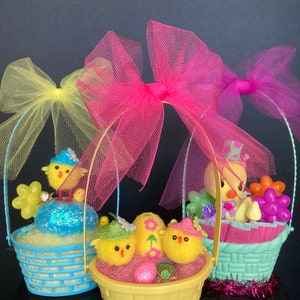 May include: Three Easter baskets decorated with yellow chicks, pastel eggs, and colorful flowers. Each basket is topped with a tulle bow in pink, yellow, or purple.