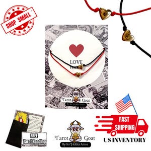 May include: Two red and black string bracelets with gold heart charms. The bracelets are displayed on a white card with the word "LOVE" printed on it. The card is surrounded by images of tarot cards. The text "Tarot Goat" is printed below the card.