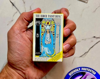 May include: A miniature Rider Tarot deck box featuring the High Priestess card illustration with a blue robe, a crescent moon, and pillars labeled B and J. The yellow box includes the text The Rider Tarot Deck and Miniature Edition.