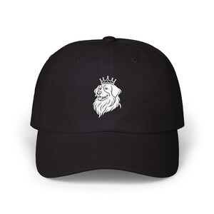 May include: Black baseball cap featuring a white illustration of a dog wearing a crown. The dog's head is in profile, with detailed fur and a smiling expression. The cap has a curved brim and a classic six-panel design.
