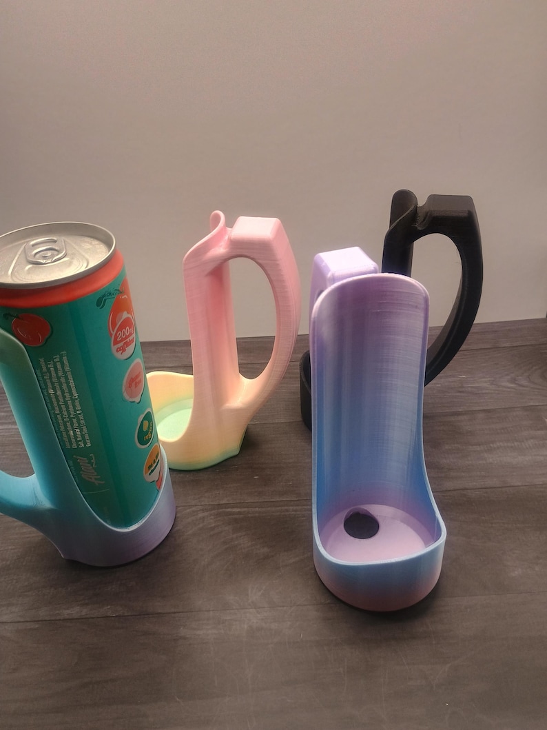 May include: A collection of 3D-printed can holders in various colors. One holder is holding a can of soda. The holders have a handle and a base to secure the can. Colors include blue, pink, purple, and black.