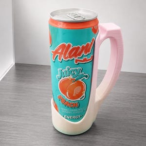 May include: A teal and orange can of Alani Nu Juicy Peach energy drink in a light pink handle. The can features the words "Alani" and "Juicy Peach" with a peach graphic. The handle is a light pink color.