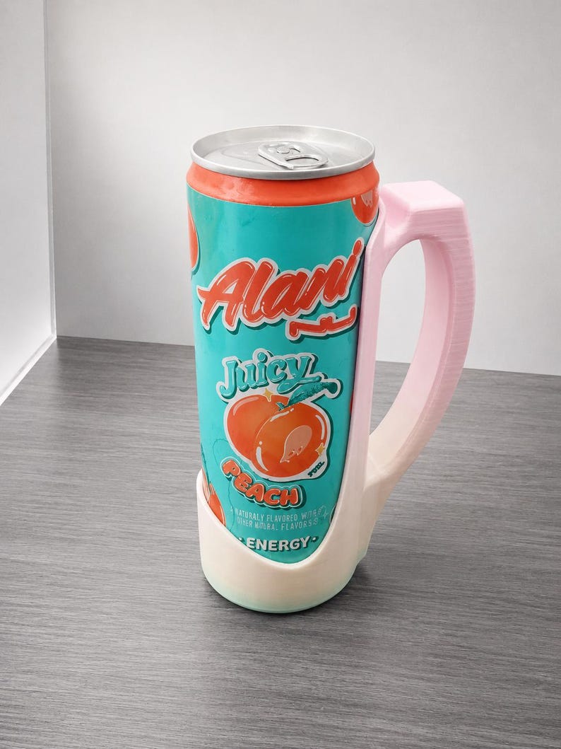 May include: A teal and orange can of Alani Nu Juicy Peach energy drink in a light pink handle. The can features the words "Alani" and "Juicy Peach" with a peach graphic. The handle is a light pink color.
