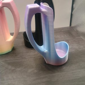 May include: Three 3D-printed, abstract-shaped objects. The front object is a gradient of blue, purple, and pink. The middle object is black, and the object on the left is a gradient of pink, yellow, and orange. All have a handle.