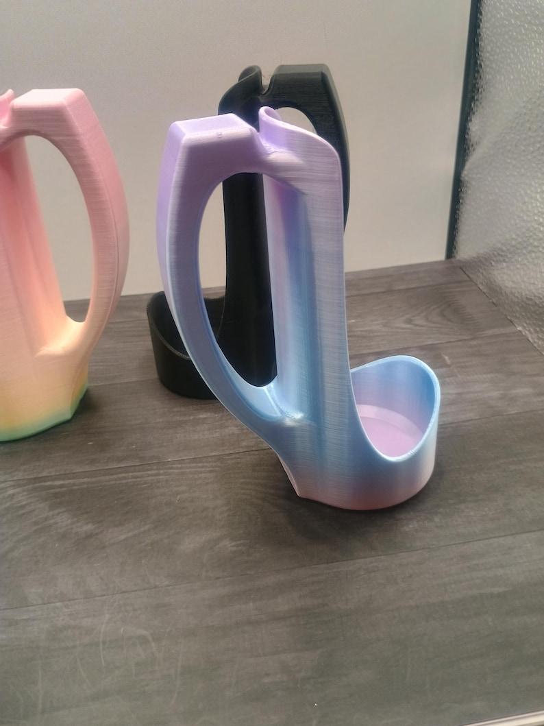 May include: Three 3D-printed, abstract-shaped objects. The front object is a gradient of blue, purple, and pink. The middle object is black, and the object on the left is a gradient of pink, yellow, and orange. All have a handle.